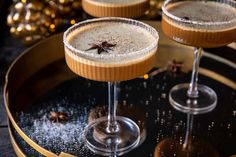 two glasses filled with drinks sitting on top of a metal tray next to christmas decorations