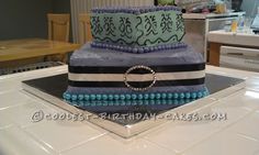 a three tiered cake is decorated with blue and black icing, beaded ring on top