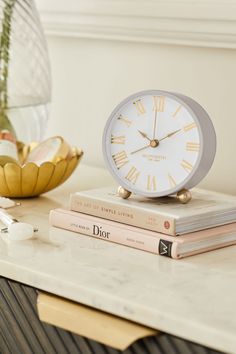 a white clock sitting on top of a table next to two books and a vase