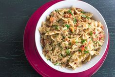 a white bowl filled with pasta and vegetables on top of a red plate next to a black table