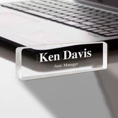 a glass business name tag sitting on top of a desk next to a laptop computer