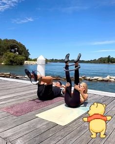 two people doing yoga on a dock near the water with winnie the pooh character