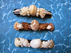 three hair pins with seashells on them sitting in the water next to each other