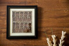 a vase with some flowers in it next to a picture frame on a wooden wall