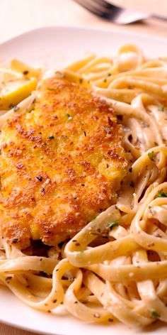 a white plate topped with pasta covered in sauce and chicken schnitzel next to a fork