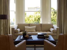 a living room with couches, chairs and tables in front of two large windows