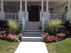 a white house with flowers in the front yard and steps leading up to the front door