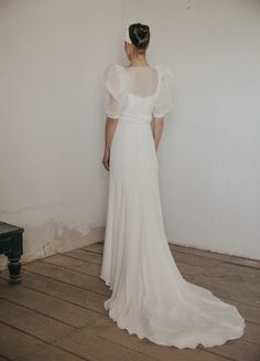 a woman in a white dress is standing against a wall with her back to the camera