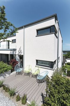 an outdoor patio with chairs and tables on the deck next to a building that has trees in front of it