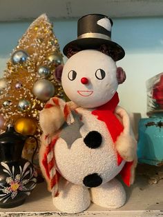 a snowman with a hat and scarf on sitting in front of a christmas tree