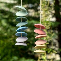 three wind chimes hanging from strings in front of trees and bushes, one with several different colored discs attached to it