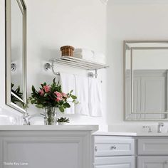 a white bathroom with two sinks, mirrors and towels on the rack over the sink