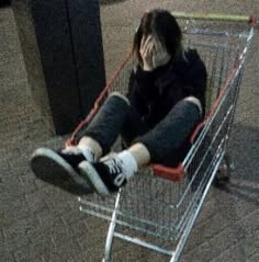 a person sitting in a shopping cart with their feet on the ground and head down