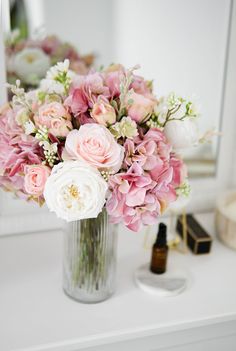 a vase filled with pink and white flowers sitting on top of a table next to a mirror