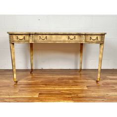 an antique console table with two drawers on one side and gold leafed legs, against a white brick wall