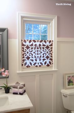 a white toilet sitting next to a bathroom sink under a window covered in decorative paper