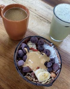 a bowl of fruit and nuts next to a cup of coffee on a wooden table