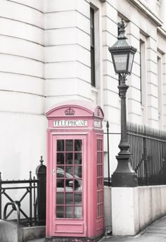 a pink phone booth sitting on the side of a street next to a lamp post