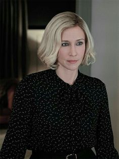 a woman with blonde hair wearing a black shirt and looking at the camera while standing in front of a door