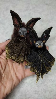 two tiny bats sitting on top of each other in someone's hand with their wings spread out