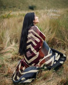 a woman is sitting in the grass wearing a blanket and looking up at the sky