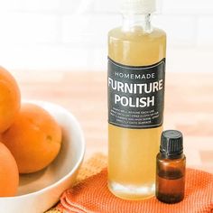 a bottle of furniture polish next to some oranges on a cloth with a bowl of oranges in the background