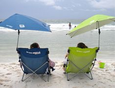 two people sitting in lawn chairs under umbrellas on the beach