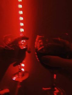 two wine glasses sitting next to each other in front of a red light filled wall