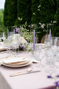 the table is set with white and purple flowers, silverware, and wine glasses