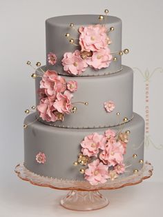 a three tiered cake with pink flowers on the side and gold beads around the edges