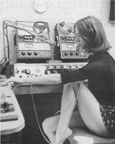 a woman sitting at a desk with headphones on her ears and radio equipment in the background