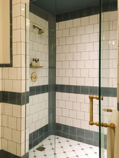 a walk in shower sitting next to a white tiled wall and floor with gold fixtures