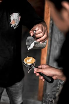 a person pouring coffee into a cup with another hand holding the cappuccino