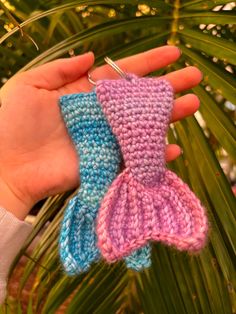 someone is holding two knitted mittens in their palm tree hands, one pink and the other blue