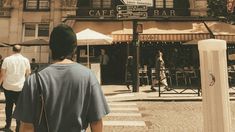 people are walking on the sidewalk in front of a cafe