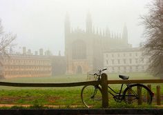 a bike parked next to a wooden fence in front of a large building on a foggy day