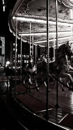 black and white photograph of two horses on a merry go round at night with people watching