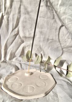 a small white vase with a plant in it on a tablecloth covered surface, next to a single twig