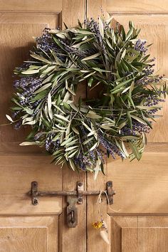 a wreath hanging on the front door of a house with lavenders and leaves around it