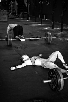 a woman laying on the ground with a barbell in front of her and another person behind her