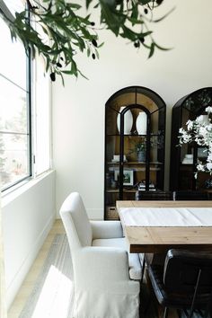 the dining room table is surrounded by white chairs and black framed china cabinets with glass doors