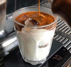 a person pouring liquid into a glass filled with ice cream and chocolate on top of an oven