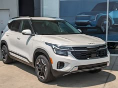 a white suv is parked in front of a building with cars on the wall behind it