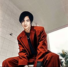 a man in a red suit and black hat sitting on a toilet with his legs crossed