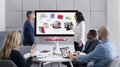 a group of people sitting around a table in front of a large screen with images on it