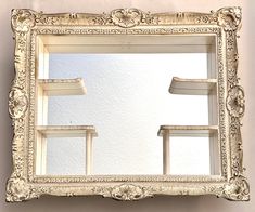 an ornate white framed mirror hanging on the wall