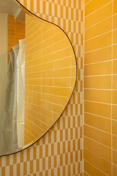 a yellow tiled bathroom with a round mirror on the wall and a white towel hanging in front of it