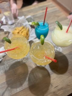 three drinks sitting on top of a wooden table next to chips and condiments