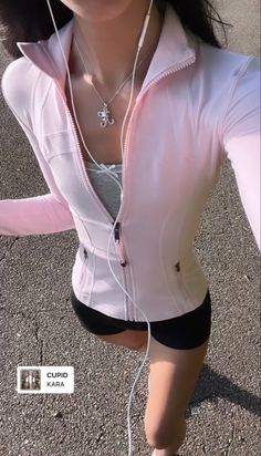 a woman with headphones on is standing in the middle of an asphalt area and wearing a pink jacket