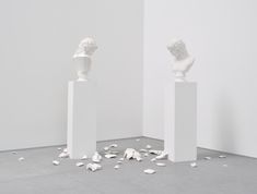 two white pedestals with sculptures in the middle and scattered petals on the floor next to them